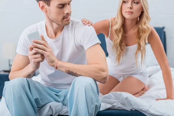 Cropped shot of jealous young woman looking at boyfriend using smartphone on bed, mistrust concept — Stock Photo