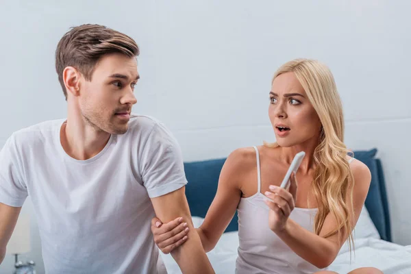 Angry woman showing smartphone to young husband sitting on bed, relationship problem concept — Stock Photo