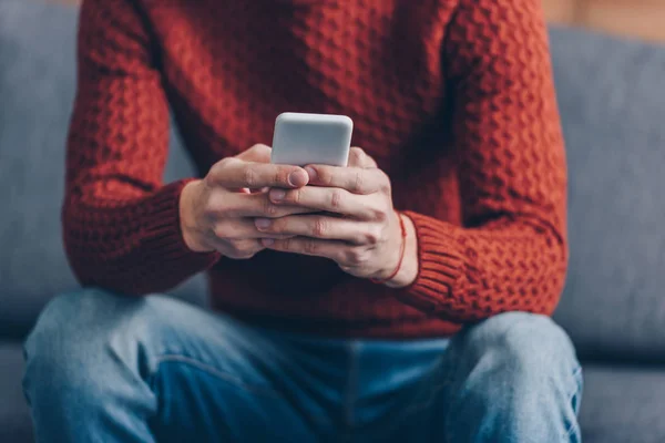 Обрезанный снимок молодого человека в красном свитере с помощью смартфона дома — стоковое фото