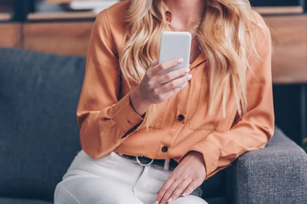 Schnappschuss einer jungen blonden Frau, die auf der Couch sitzt und ihr Smartphone benutzt — Stockfoto