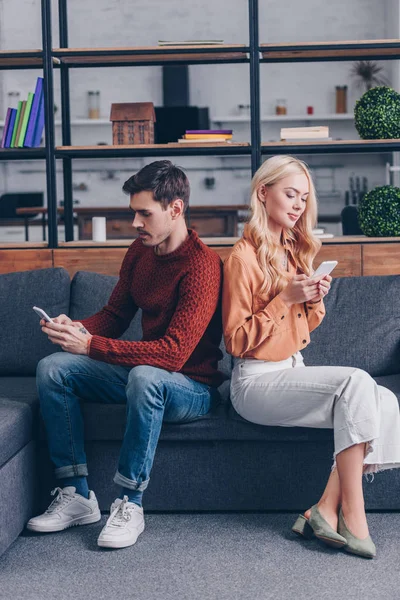 Junges Paar, Rücken an Rücken sitzend und Smartphones nutzend, Beziehungsproblemkonzept — Stockfoto