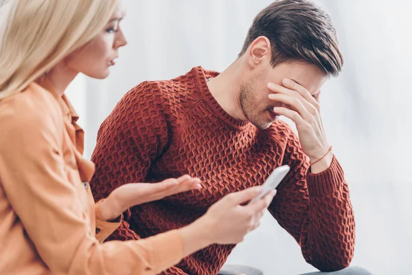 Jealous young woman showing smartphone to upset husband at home, distrust concept — Stock Photo