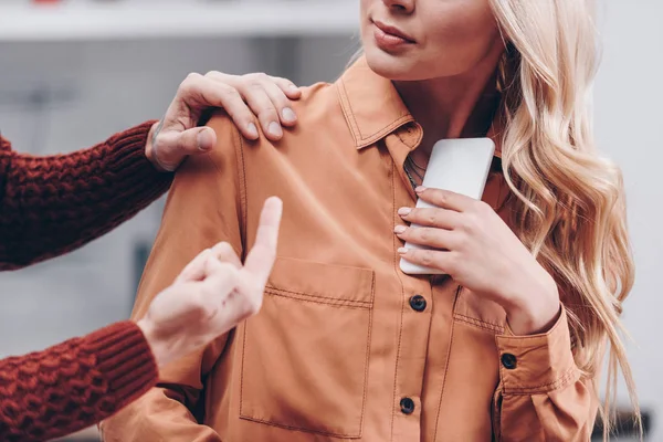 Обрезанный снимок мужчины, указывающего пальцем на молодую жену, держащую смартфон, концепция недоверия — стоковое фото