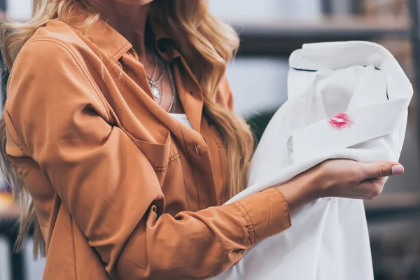 Partial view of girl holding white male shirt with lipstick traces, betrayal concept — Stock Photo