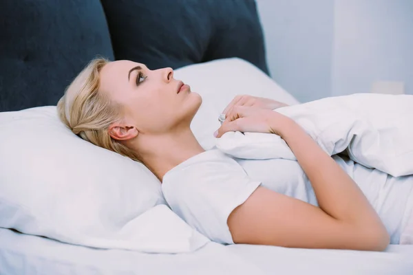 Mujer triste sosteniendo la manta mientras está acostado en la cama en casa — Stock Photo