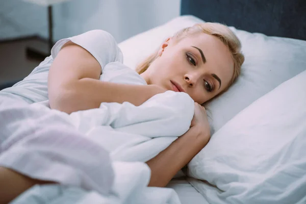 Selective focus of upset woman holding blanket while lying in bed at home — Stock Photo