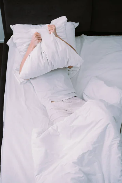 Подавленная женщина покрывает лицо подушкой, лежа в постели дома — стоковое фото