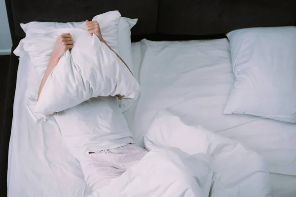 Mujer deprimida cubriendo la cara con almohada mientras está acostada en la cama en casa - foto de stock