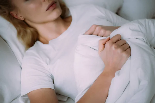 Vista cortada da mulher de pijama branco deitado na cama e segurando cobertor — Fotografia de Stock