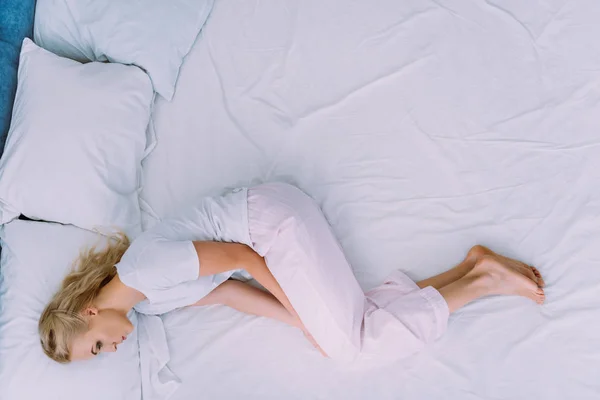 Депрессивная женщина в белой пижаме лежит в постели с копировальным пространством — стоковое фото