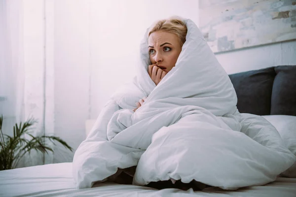Frightened woman covered in blanket biting hand in bed at home — Stock Photo