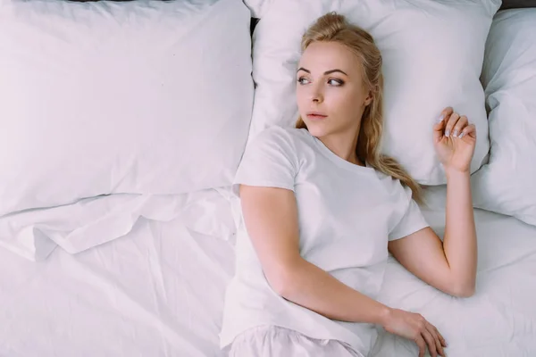 Депресивна жінка в білій піжамі лежить в ліжку з копіювальним простором — стокове фото