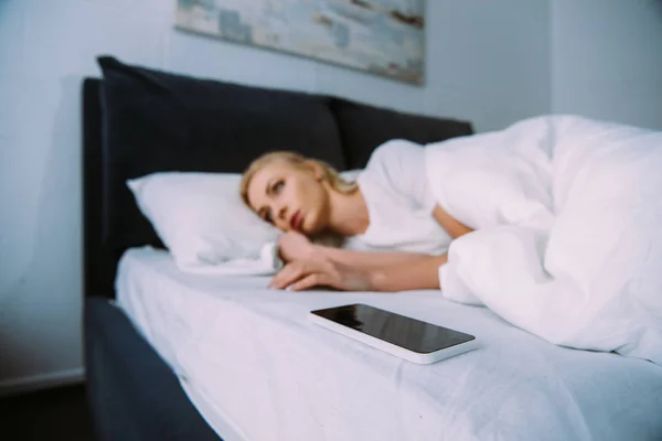 Mujer molesta acostada con teléfono inteligente en la cama en casa - foto de stock