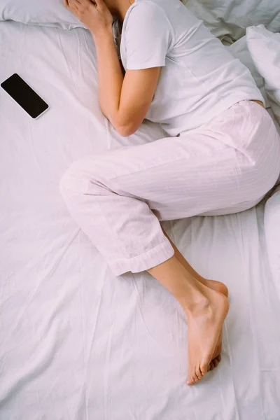 Cropped view of woman lying near smartphone with blank screen in bed at home — Stock Photo