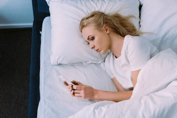 Triste mujer solitaria acostada en la cama y el uso de smartphone - foto de stock