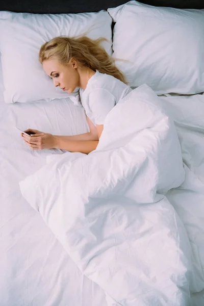 Traurige einsame Frau liegt im Bett und benutzt Smartphone — Stockfoto