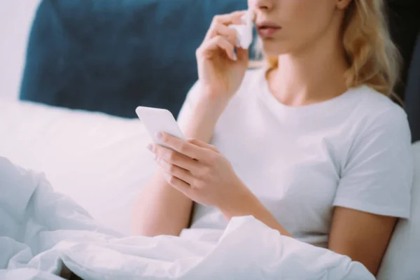 Abgeschnittene Ansicht einer Frau, die sich Tränen abwischt und ihr Smartphone zu Hause im Bett benutzt — Stockfoto