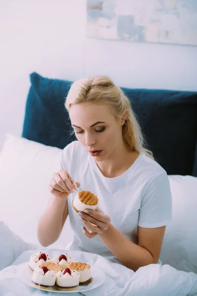 Bela mulher triste em pijama branco comer bolo na cama sozinho — Fotografia de Stock