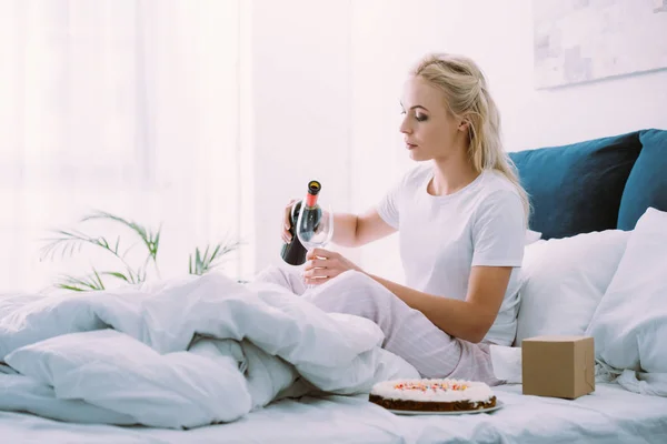 Sad woman pouring wine in glass while celebrating birthday in bed alone — Stock Photo