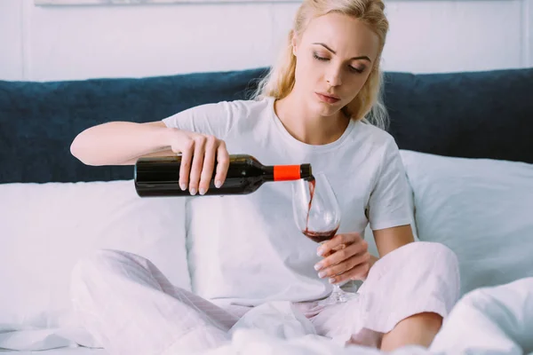 Mulher triste em pijama derramando vinho tinto na cama em casa — Fotografia de Stock