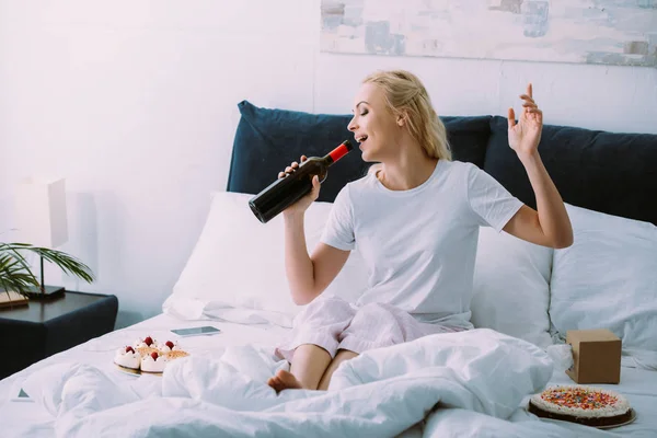 Glückliche Frau trinkt Wein, während sie Geburtstag allein im Bett feiert — Stockfoto