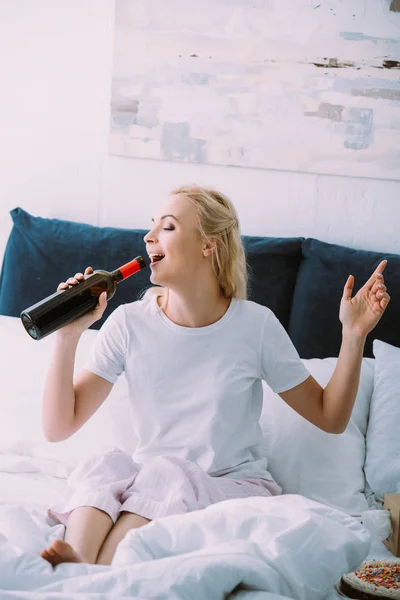 Belle femme souriante en pyjama boire du vin au lit à la maison — Photo de stock