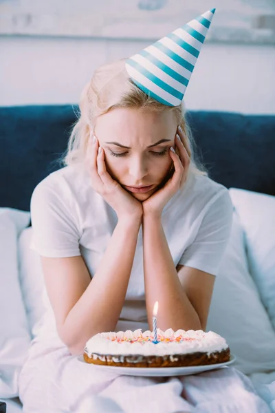 Depressive Frau schaut Kuchen an, während sie Geburtstag allein im Bett feiert — Stockfoto