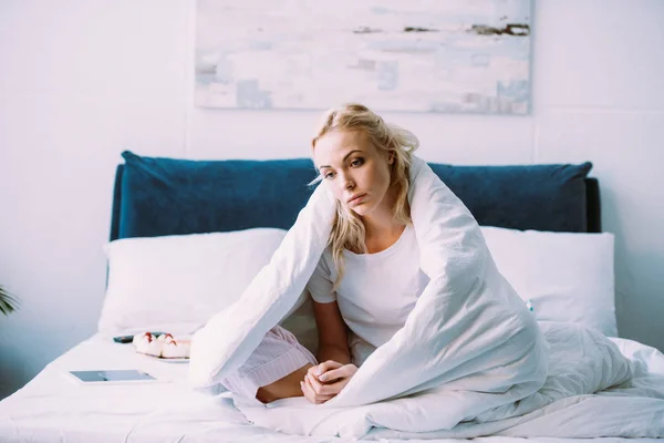 Селективное внимание грустной одинокой женщины, покрытой одеялом, сидящей дома на кровати — стоковое фото