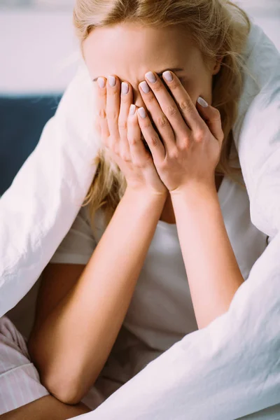 Selektiver Fokus der Frau in einer Decke, die das Gesicht mit den Händen bedeckt und zu Hause im Bett weint — Stockfoto