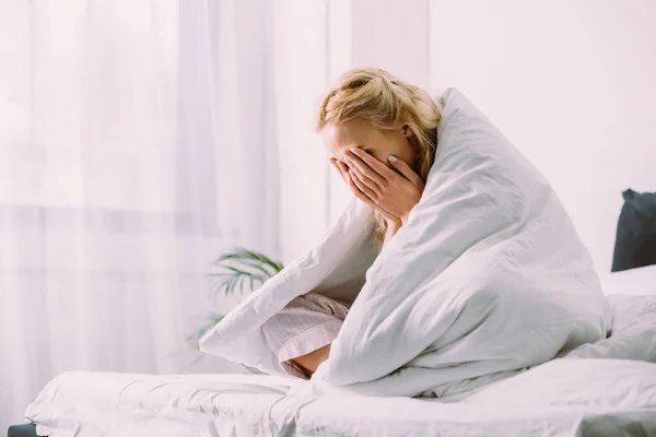 Mulher em cobertor cobrindo rosto com as mãos e chorando na cama em casa — Fotografia de Stock