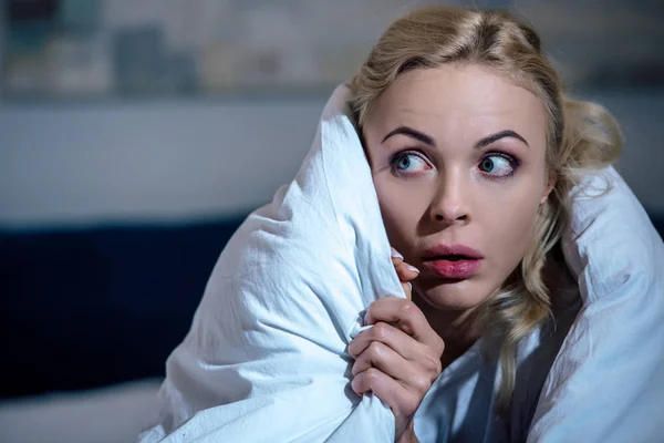 Selective focus of frightened woman covered in blanket looking away in bedroom — Stock Photo