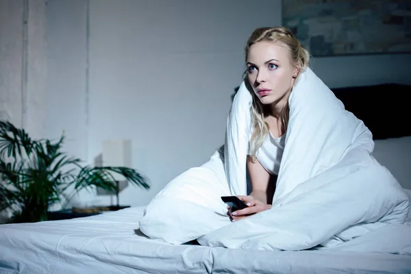 Одинокая женщина, покрытая одеялом, смотрит телевизор в постели дома — стоковое фото