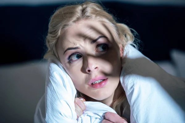 Selective focus of frightened woman covered in white blanket looking away — Stock Photo