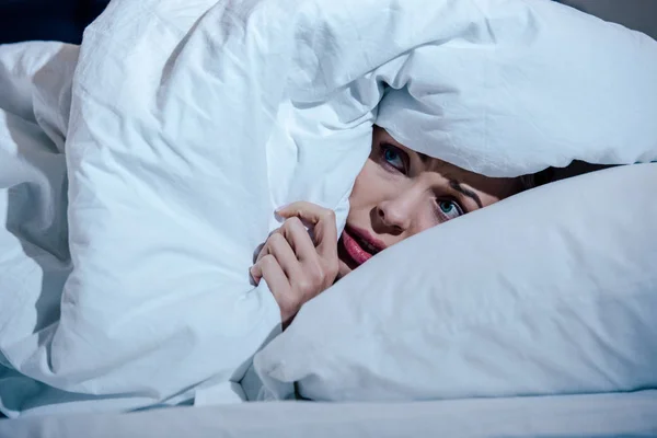 Scared woman hiding behind blanket in bedroom at home — Stock Photo