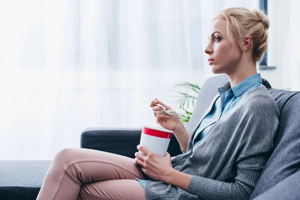 Femme triste manger de la crème glacée tout en siitng sur le canapé à la maison seul avec l'espace de copie — Photo de stock