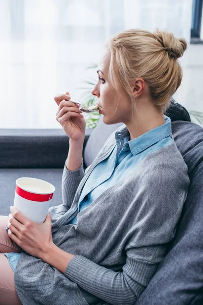 Пригнічена жінка їсть морозиво під час перебування на дивані вдома одна — стокове фото