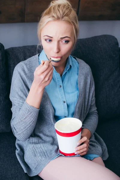 Traurige Frau isst Eis, während sie allein zu Hause auf der Couch sitzt — Stockfoto