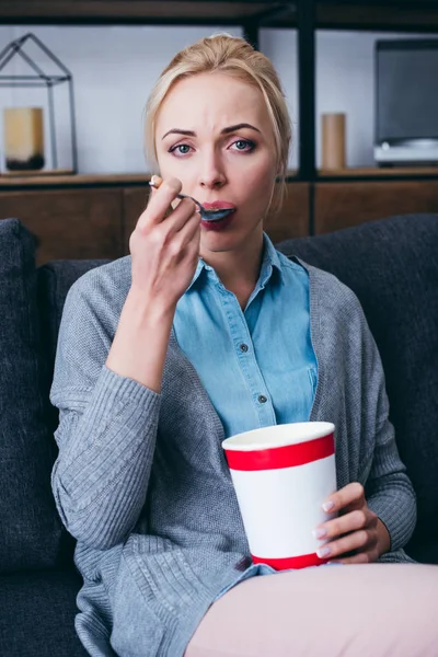 Femme triste regardant caméra et manger de la crème glacée tout en siitng sur le canapé à la maison seul — Photo de stock