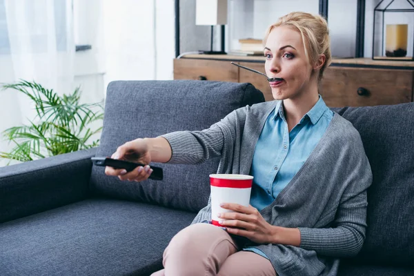 Woman eating ice cream while siitng on couch and wathicng tv at home alone — Stock Photo