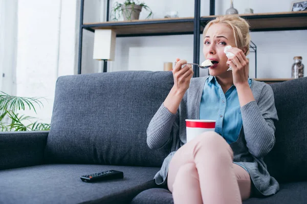 Woman eating ice cream and crying while siitng on couch and watching tv at home alone — Stock Photo