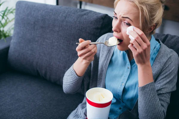 Woman eating ice cream and crying while siitng on couch at home alone — Stock Photo