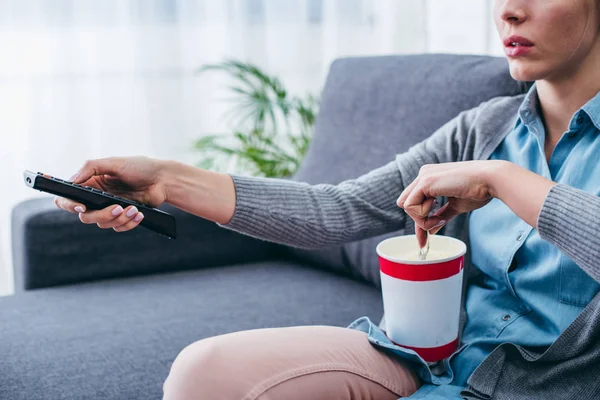 Vista ritagliata della donna seduta sul divano con gelato e telecomando mentre guarda la tv — Foto stock