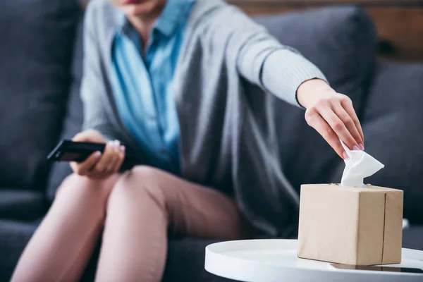 Ausgeschnittene Ansicht einer Frau auf der Couch, die zu Hause nach einer Gewebebox greift — Stockfoto