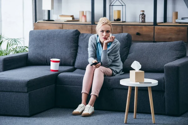 Triste mulher sentado no sofá com balde de sorvete e caixa de tecido enquanto assiste tv na sala de estar — Fotografia de Stock