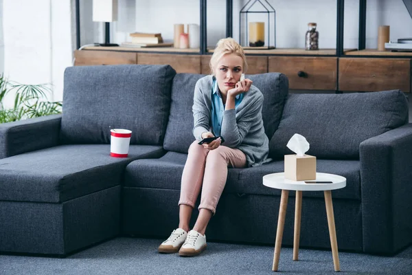 Femme triste assis sur le canapé avec seau de crème glacée et boîte de tissu tout en regardant la télévision dans le salon — Photo de stock