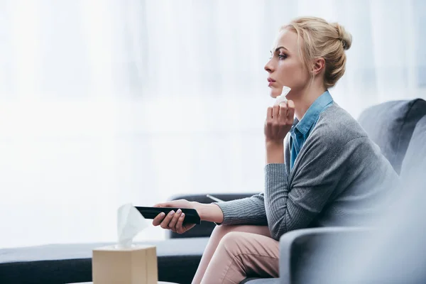 Upset woman with tissue watching tv on couch at home alone — Stock Photo