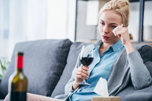 Mulher chateada com copo de vinho chorando e enxugando lágrimas com tecido em casa — Fotografia de Stock