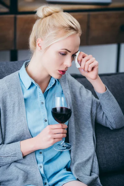 Upset woman with glass of wine crying and wiping tears with tissue at home — Stock Photo