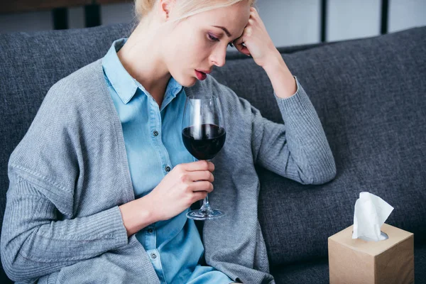 Upset woman sitting with glass of red wine and tissue box at home — Stock Photo