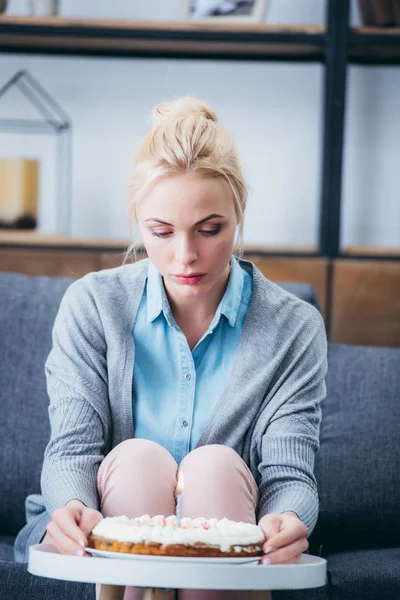 Depressed woman holding cake while celebrating birthday at home alone — Stock Photo